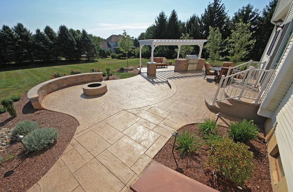 Stamped concrete patio with curved seating wall, fire pit, and pergola in a landscaped Easton, Pennsylvania backyard