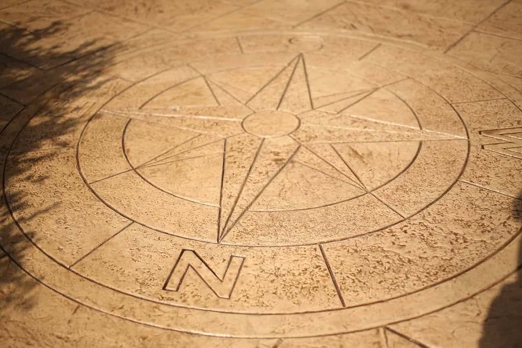 Stamped concrete patio featuring a decorative compass rose design with engraved directional details and natural stone texture.