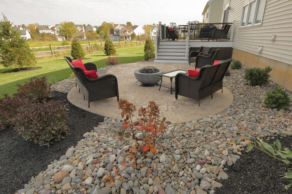 A firepit area on a stamped concrete buff colored stamped concrete patio with a deck step entrance leading to another area of the backyard design