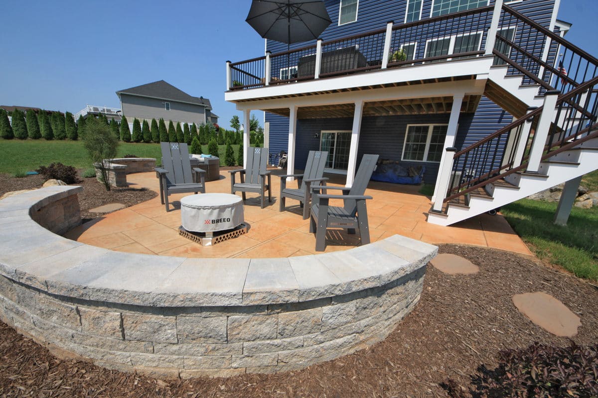 Stamped concrete patio with curved seating wall and fire pit designed by Signature Landscape Design