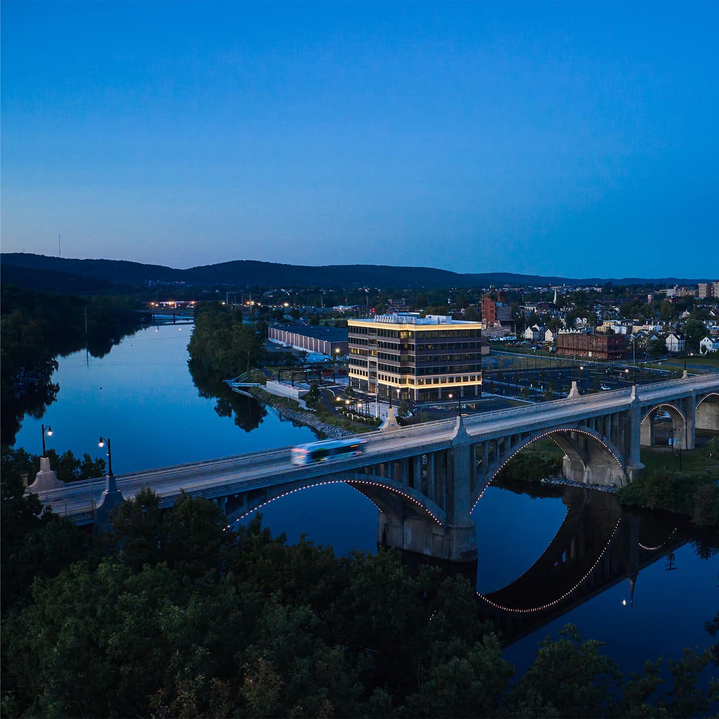 Aerial view of The Waterfront at dusk, with 615 Waterfront lit beside the Lehigh River in Allentown.