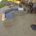 A large outdoor kitchen sits atop a seamless textured concrete patio