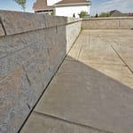 A champlain gray colored Techo Bloc wall and a buff colored stamped concrete patio next to each other