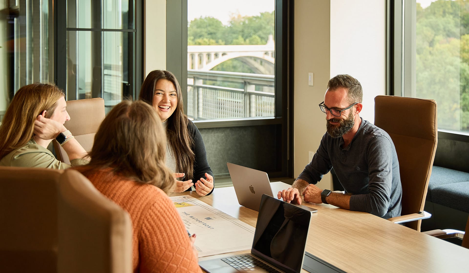 Coworkers reviewing work on laptops beside bridge-view windows at 615 Waterfront
