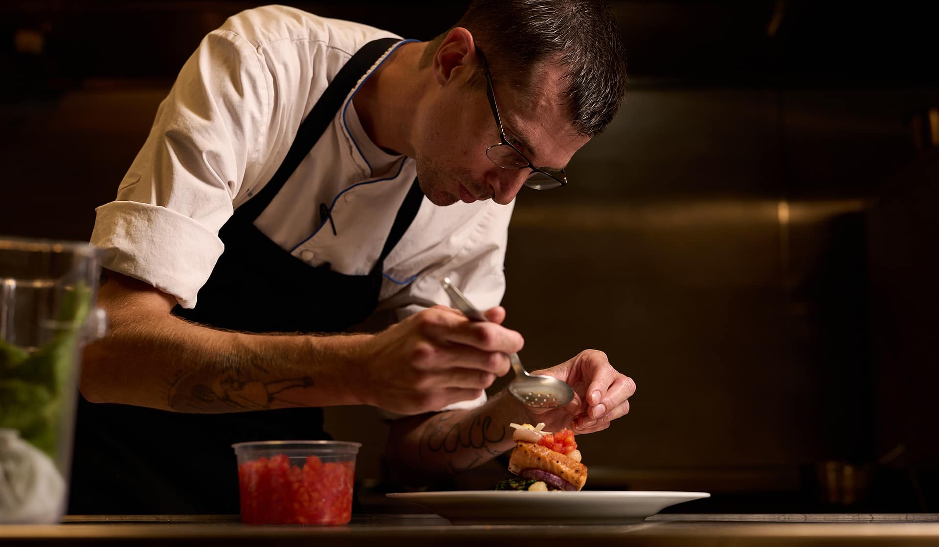 Chef Tyler garnishing a plated dish in the kitchen at Nowa at The Waterfront