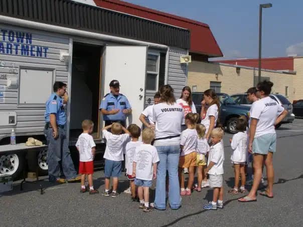 Children and adults stand next to white trailer. 